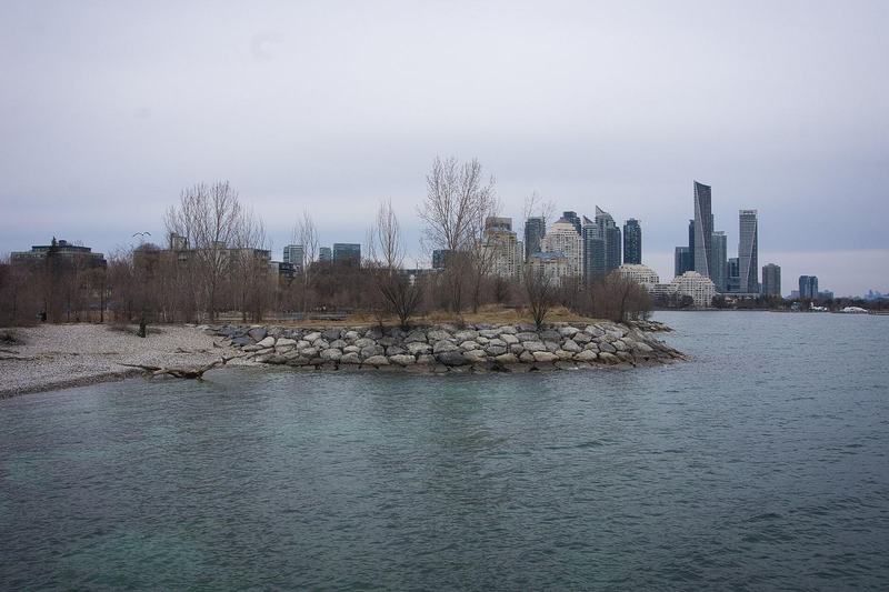 Mimico Waterfront Park shoreline with rocks, bare trees and the Humber Bay Shores towers across the water