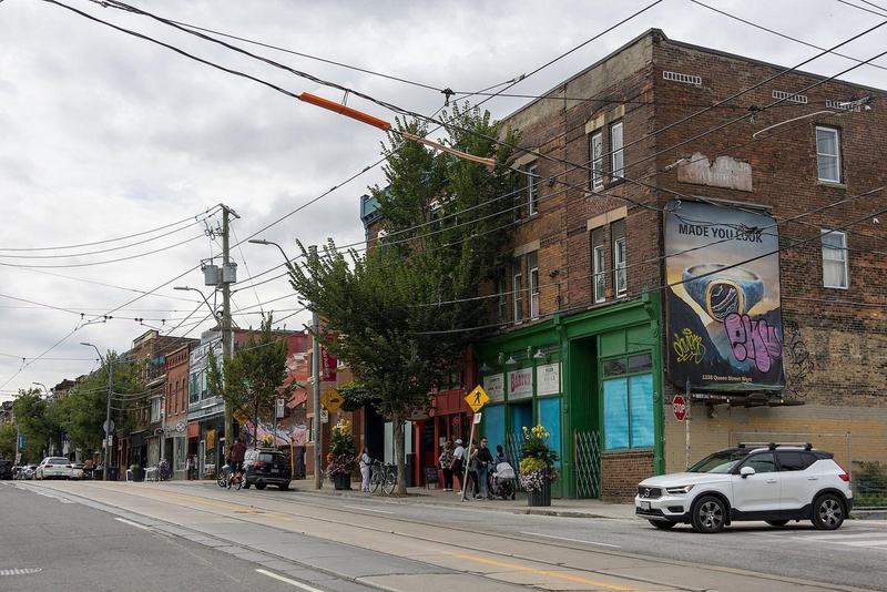 Queen Street West at Noble Street in Parkdale, Toronto, with shops, trees and streetcar tracks