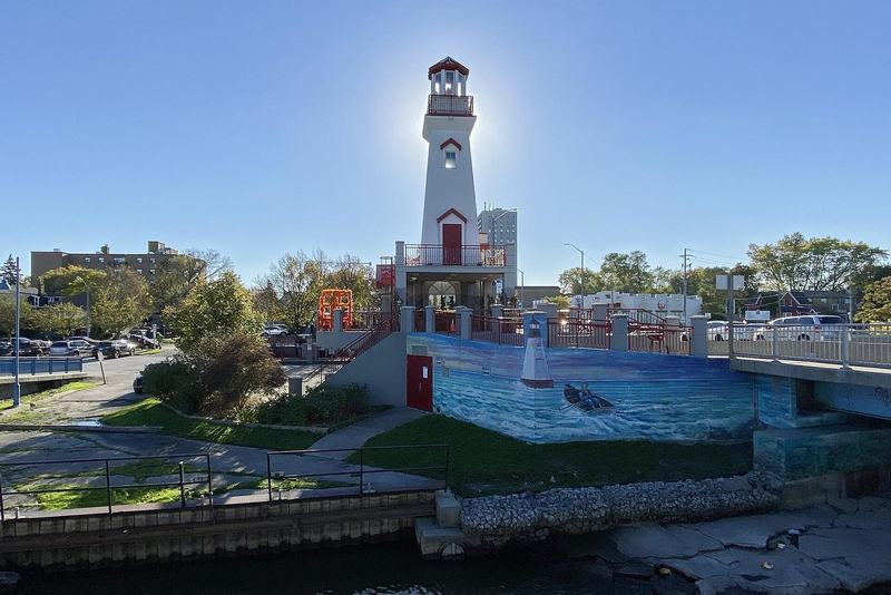 The Port Credit Lighthouse beside the harbour in Mississauga, Ontario, with a blue sky and a painted fish mural